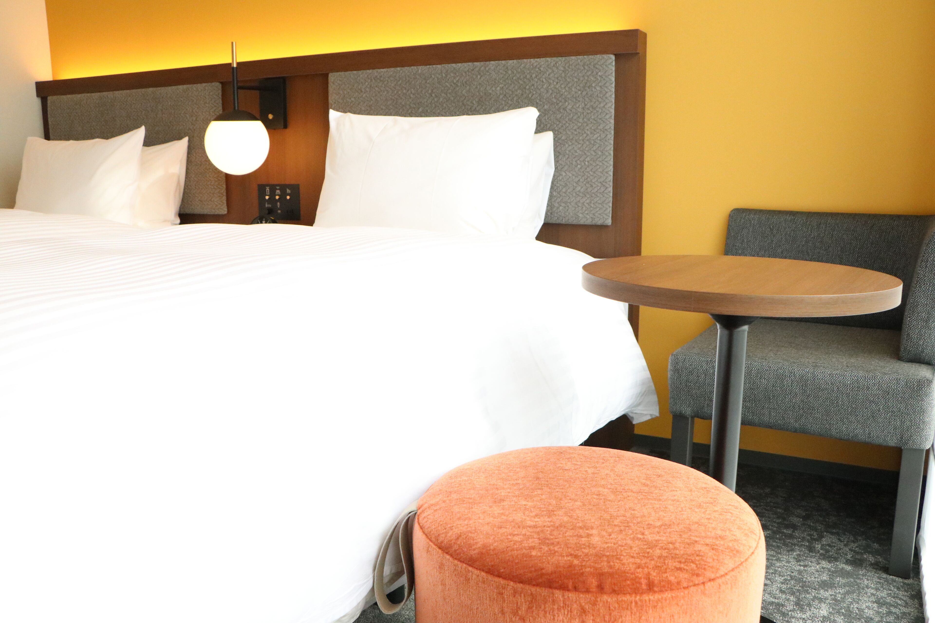 Une chambre d’hôtel avec un grand lit, une table ronde et un fauteuil gris.