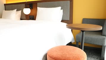 Une chambre d’hôtel avec un grand lit, une table ronde et un fauteuil gris.