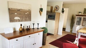 Una sala de estar con una mesa de centro de madera, sillas rojas, un armario blanco y una zona de cocina al fondo.