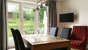 A dining area with a table set for four, chairs, a television mounted on the wall, and a view of a garden through the glass door.