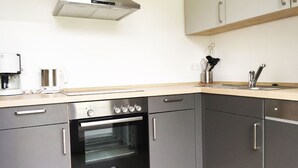 A modern kitchen with grey cabinets, a built-in oven, a coffee maker, and a stainless steel range hood.