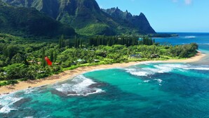 Un paisaje costero con una playa, aguas turquesas cristalinas y montañas verdes exuberantes al fondo.