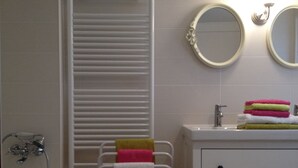 Un baño con un lavamanos blanco, dos espejos, un perchero para toallas con varias toallas y una toalla colgando.