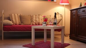Una sala de estar acogedora con un sofá rojo, una mesita blanca con una botella y vasos, y un aparador de madera.
