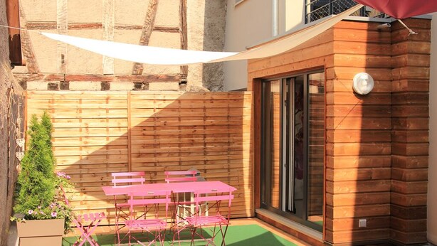 Un patio con una mesa y sillas de madera, un tapete verde y una valla de madera.