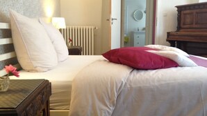 Una cama bien hecha con almohadas blancas y rojas, una mesita de noche con una lámpara y un aparador de madera.