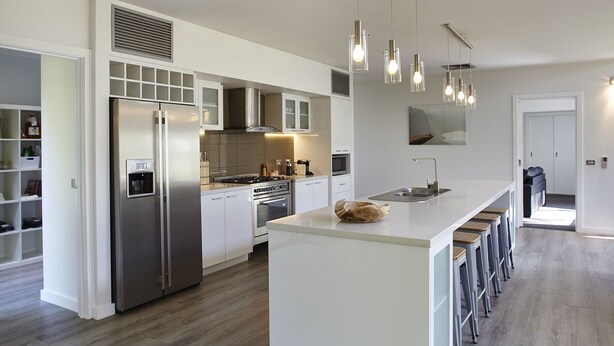 Cozinha moderna com ilha central, eletrodomésticos de aço inoxidável e área de bar com banquetas.