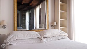 Quarto com um espelho grande, uma cama com roupa de cama branca e um aparador na parede.
