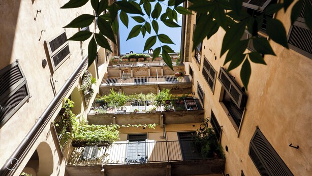 Um edifício com vários andares e varandas, algumas com plantas, e um céu claro visível pelas janelas.