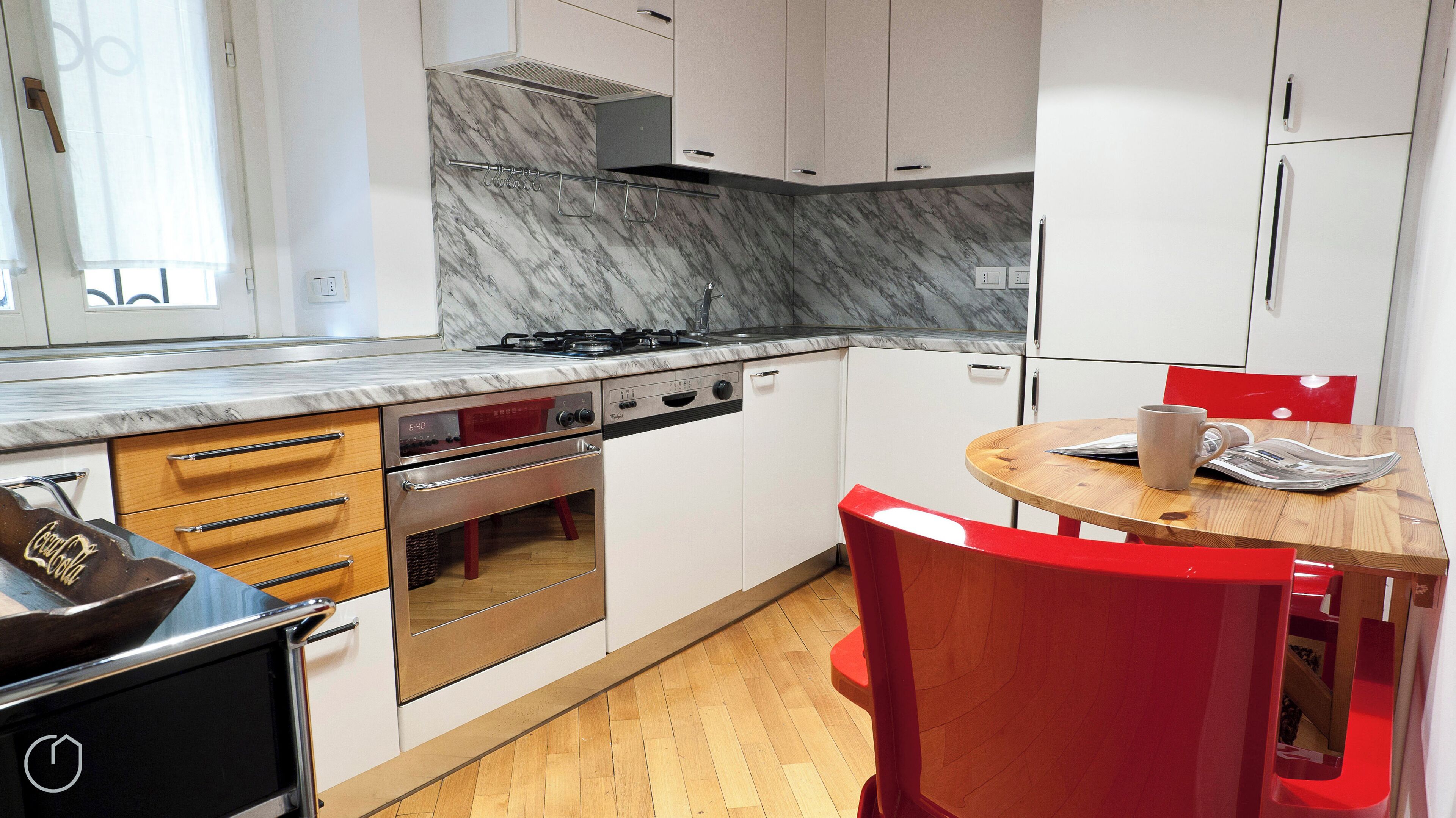 A modern kitchen with white cabinets, a stove, and a wooden dining table with red chairs.