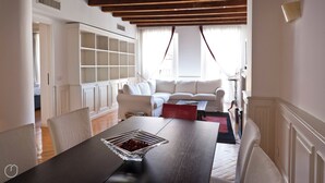 Ampla sala de estar com mesa de jantar, sofás brancos e estante embutida.