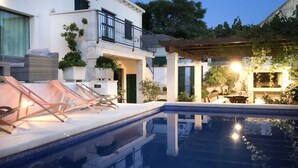 En swimmingpool med solstolar, en pergola och en vit byggnad med en balkong.