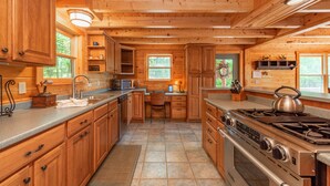 A wooden cabin kitchen with a stove, microwave, and wooden cabinets. - Mountain Lodge w/ Fire Pit, Games & Lake Fun (Swanton)