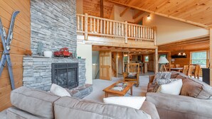A spacious living area with a stone fireplace, wooden furniture, and a balcony with a wooden railing. - Mountain Lodge w/ Fire Pit, Games & Lake Fun (Swanton)
