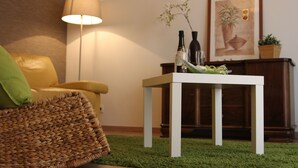 A room with a yellow armchair, a white table with a bottle and glass, a lamp, and a framed picture on the wall. - Cottage LE PATIO (Wasselonne)