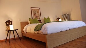 A bedroom with a wooden bed, green and white pillows, a framed picture on the wall, and a radiator. - Cottage LE PATIO (Wasselonne)
