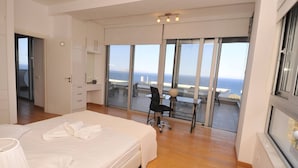 Un dormitorio moderno con una cama grande, un escritorio y vistas al océano a través de ventanales.