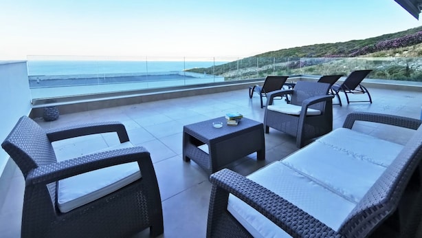 Una terraza con mobiliario de mimbre, vista al mar y una colina al fondo.
