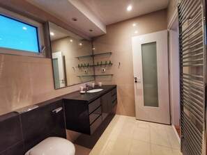 A modern bathroom with a dark countertop sink, a white toilet, and a glass shower enclosure.