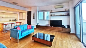 Una sala de estar moderna con un sofá azul, una mesa de centro de vidrio y un televisor sobre un mueble de madera.