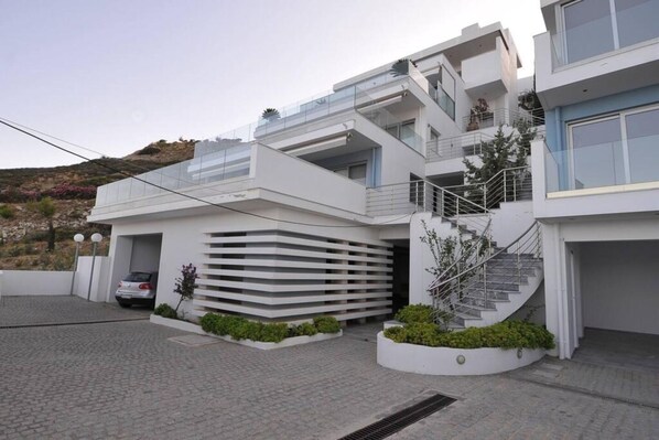 A modern multi-story residential building with a garage, a staircase, and a landscaped area with plants.