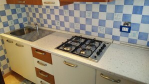 Une cuisine de taille réduite, équipée d’une cuisinière à gaz, d’un évier et d’un crédence à carreaux.