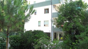 Un immeuble à plusieurs étages doté de balcons, entouré d’une végétation luxuriante.