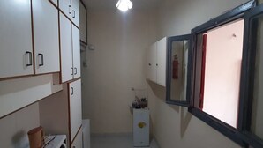 A narrow hallway with white cabinets, a small white appliance, and a window with a red frame. - Monatop  Studio Furn El Chebbek (Forn El Chebbak)