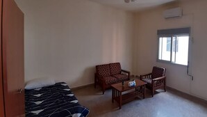 A room with a bed, two patterned sofas, a small table, and a window with blinds. - Monatop  Studio Furn El Chebbek (Forn El Chebbak)