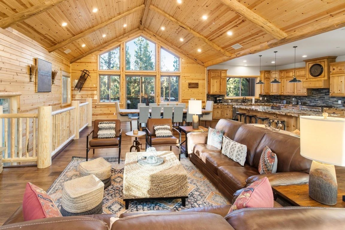 A spacious living area with a large wooden ceiling, a brown leather sofa, and a dining table with chairs.
