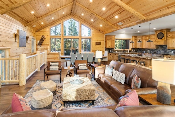 A spacious living area with a large wooden ceiling, a brown leather sofa, and a dining table with chairs.