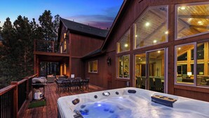 Ein Holzhaus mit Whirlpool auf der Terrasse, einer überdachten Veranda und großen Fenstern.