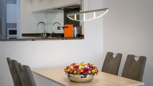 Una cocina moderna con horno integrado, un lavamanos y una luz de techo brillante. En primer plano, una mesa de comedor con un colorido arreglo floral.