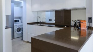 Una cocina moderna con armarios blancos, encimera oscura y lavadora integrada.