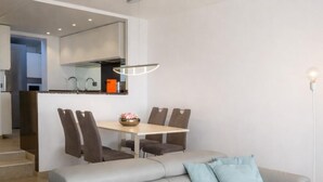 Una sala de estar moderna con un sofá gris, una mesa de comedor con sillas y una zona de cocina al fondo.