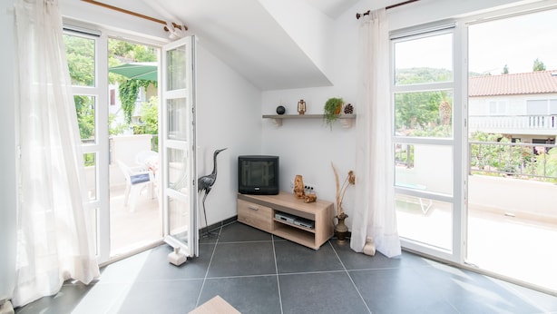 A bright living room with a TV, shelves with plants, and a view of the outdoors. - Apartments Mare (Postira)