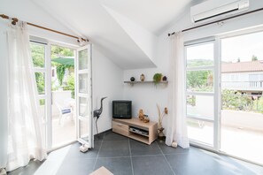 A bright living room with a TV, shelves with plants, and a view of the outdoors. - Apartments Mare (Postira)