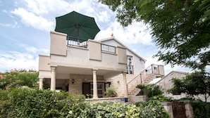 A two-story house with a covered porch, a staircase, and a green umbrella. - Apartments Mare (Postira)