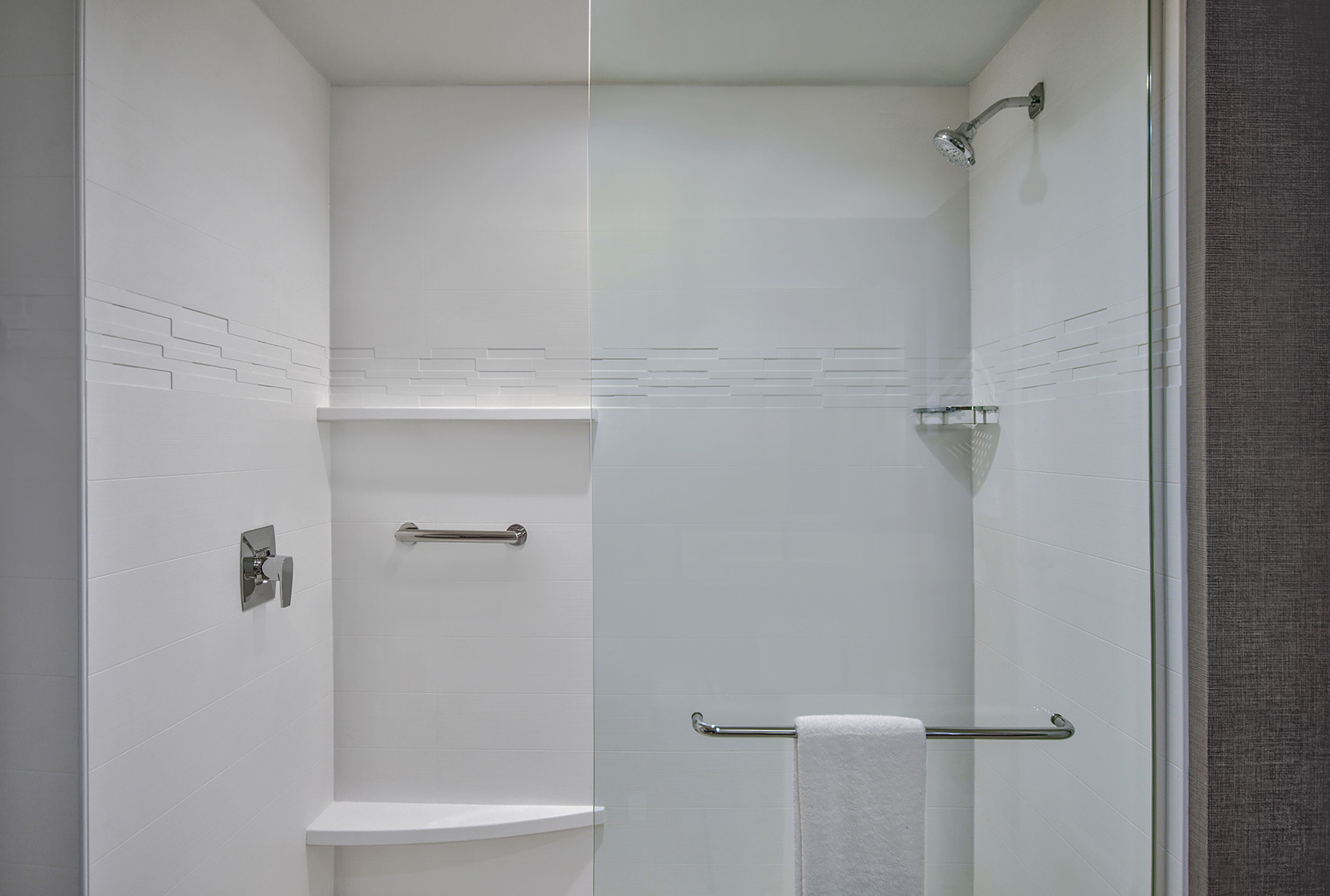 A modern shower with a glass door, a white tiled wall, and a towel rack.