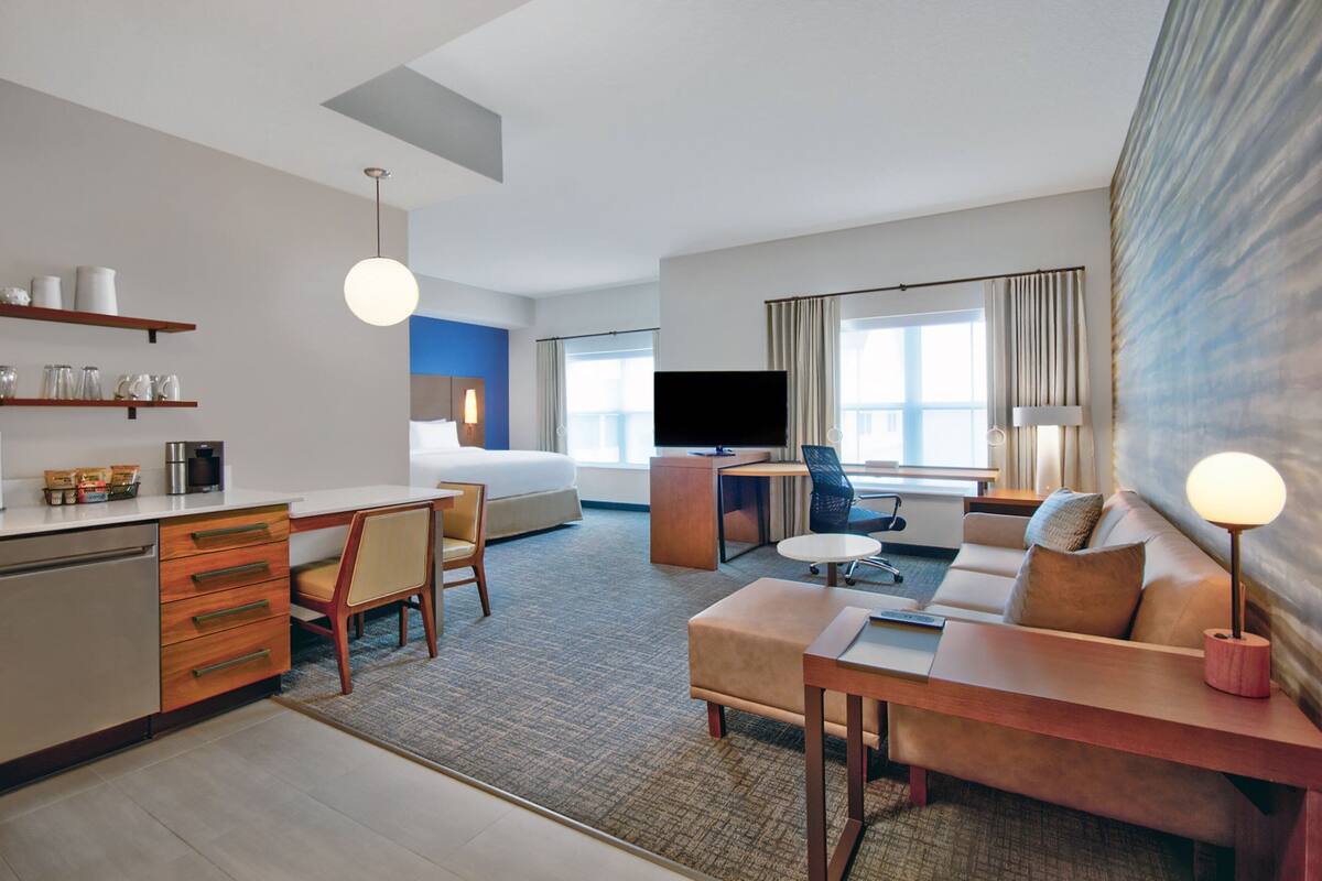 Una habitación de hotel moderna con kitchenette, una cama, un escritorio, un sofá y un televisor.
