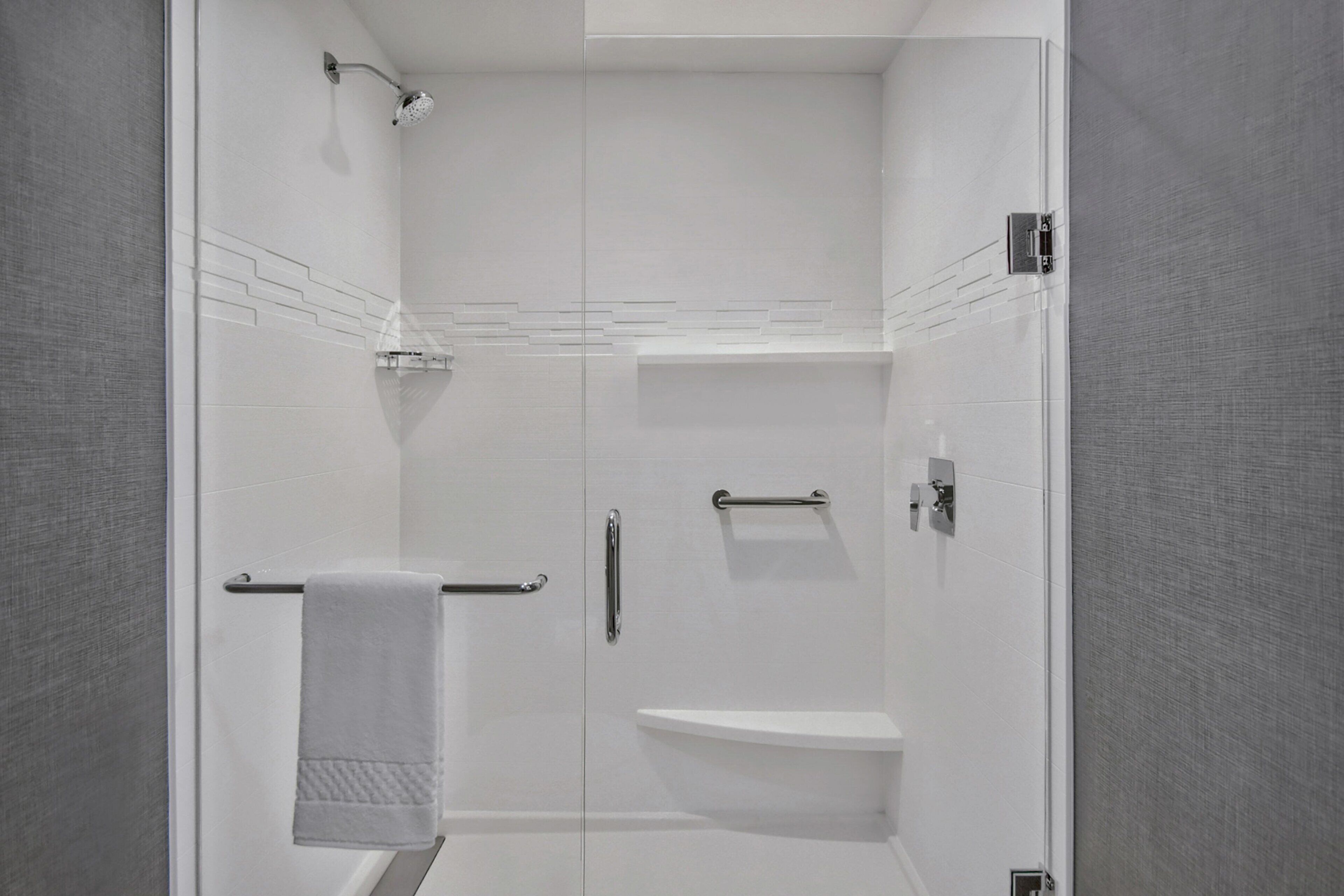 Un baño moderno con cabina de ducha de vidrio, una toalla blanca y un estante empotrado.