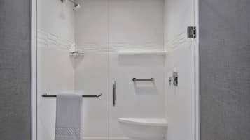 Un baño moderno con cabina de ducha de vidrio, una toalla blanca y un estante empotrado.