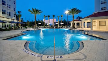 A swimming pool with a central pole, surrounded by lounge chairs and palm trees.
