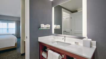 Une chambre d’hôtel avec un grand lit, un meuble-lavabo blanc avec un miroir et une fenêtre avec des rideaux.