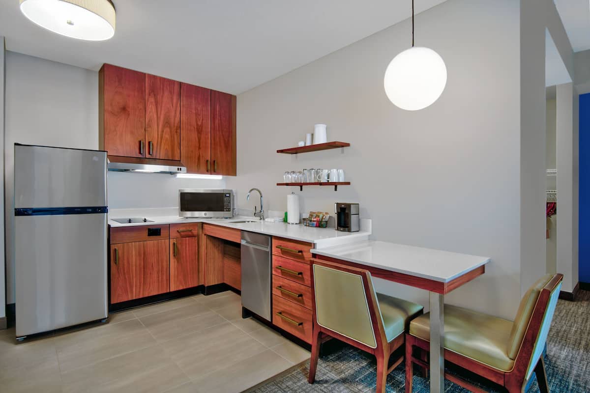 Una cocina moderna con armarios de madera, electrodomésticos de acero inoxidable, una encimera blanca y un comedor con mesa y sillas.