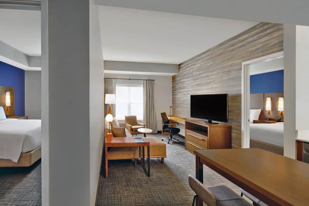 Habitación de hotel con una cama, un escritorio con silla, un televisor y un baño visible a través de una puerta abierta.