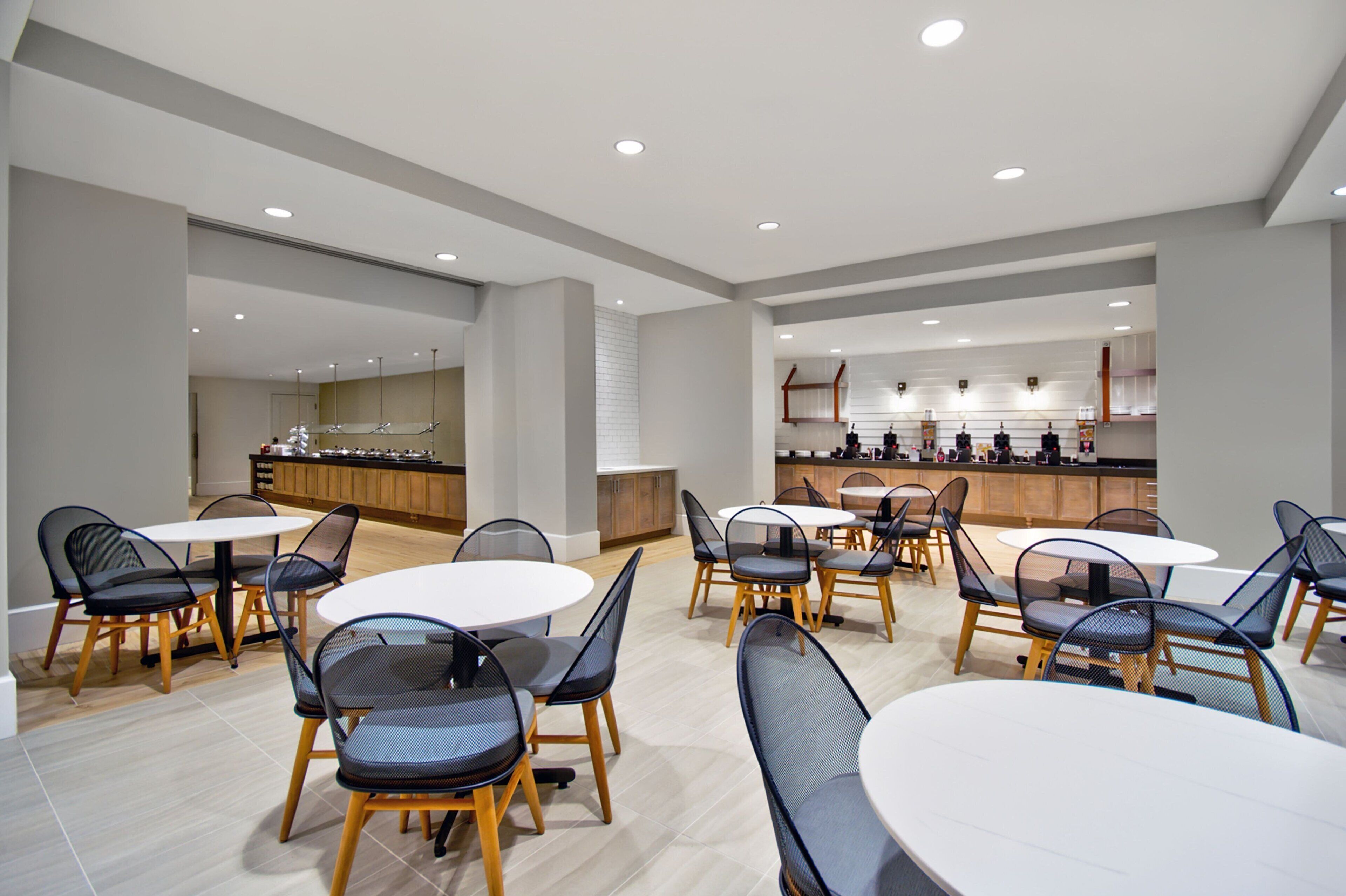 Un espace repas moderne avec des tables et des chaises rondes, une cuisine en arrière-plan et un design épuré et minimaliste.