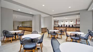 Un espace repas moderne avec des tables et des chaises rondes, une cuisine en arrière-plan et un design épuré et minimaliste.