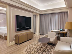 Hotellihuone, jossa on sänky, televisio, työpöytä tietokoneella, tuoli ja sohvapöytä.