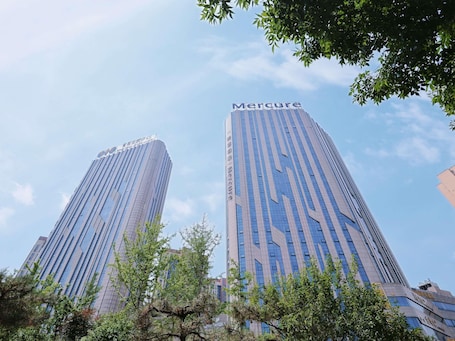 Two tall buildings with the name 'Mercure' on top, surrounded by trees.. Mercure Anyang Downtown